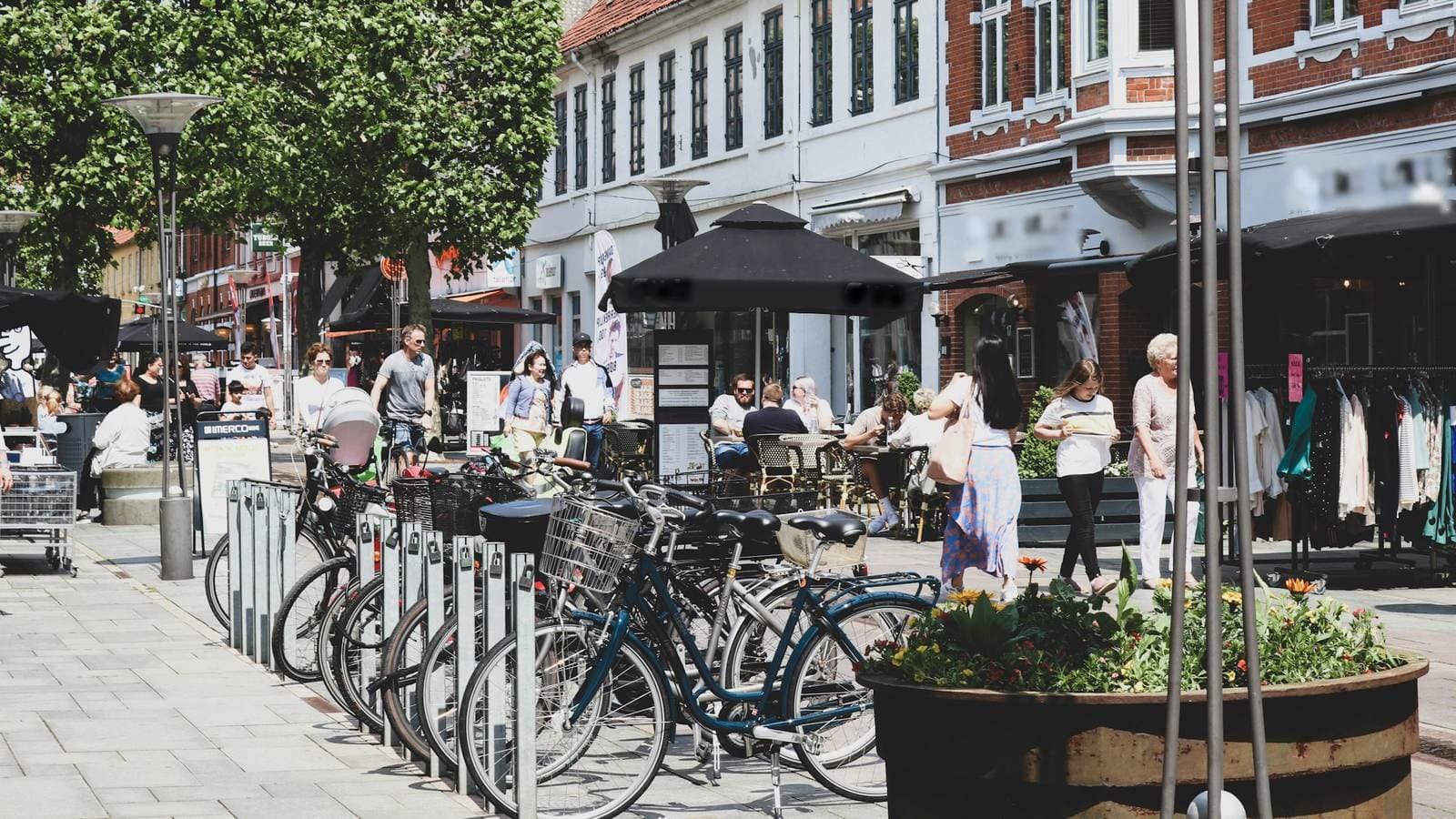 Gågade i en dansk provinsby med små butikker, parkerede cykler og mennesker på afstand