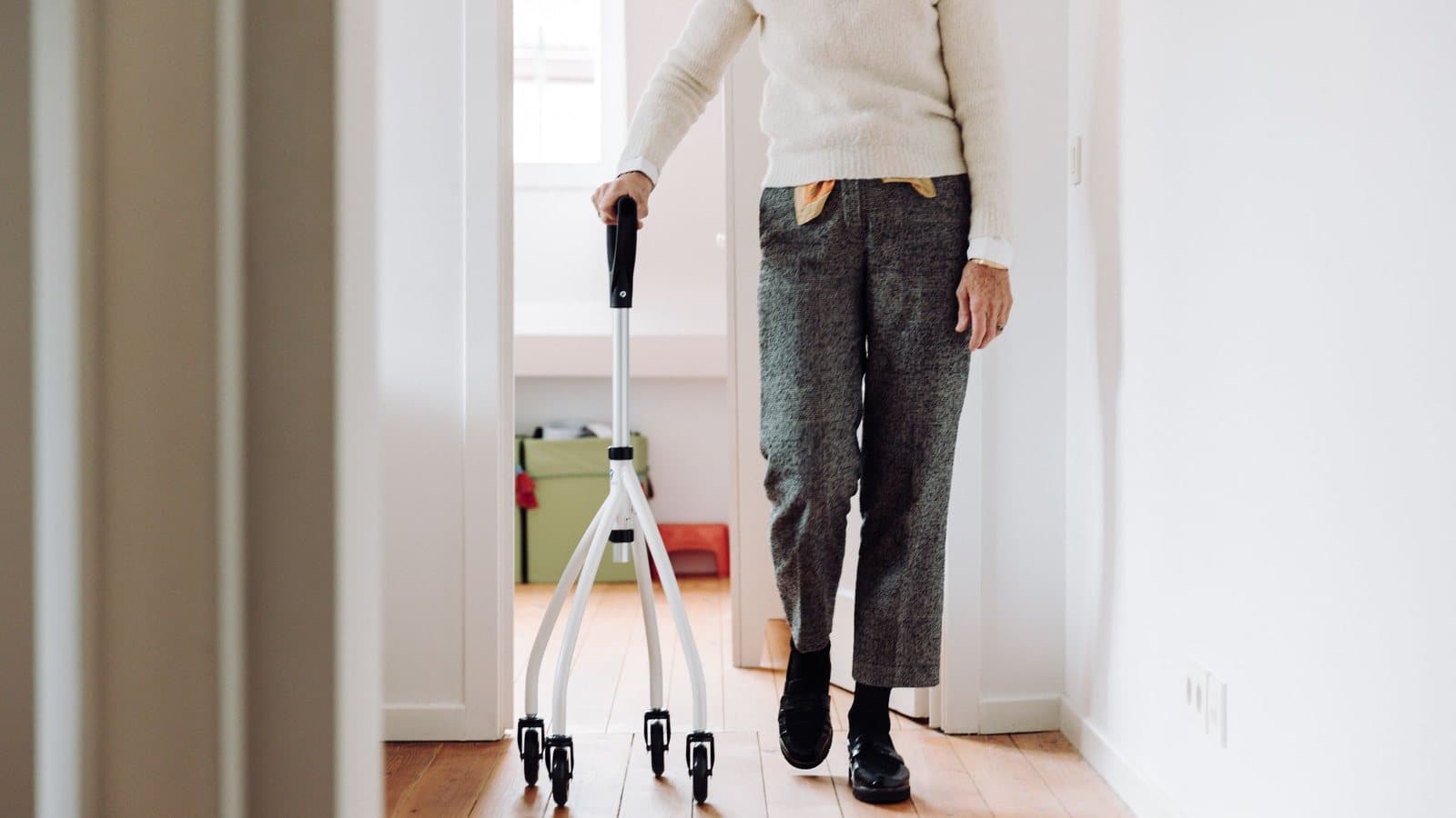 Ældre kvinde går gennem en lys entré derhjemme og støtter sig til et ganghjælpemiddel på hjul